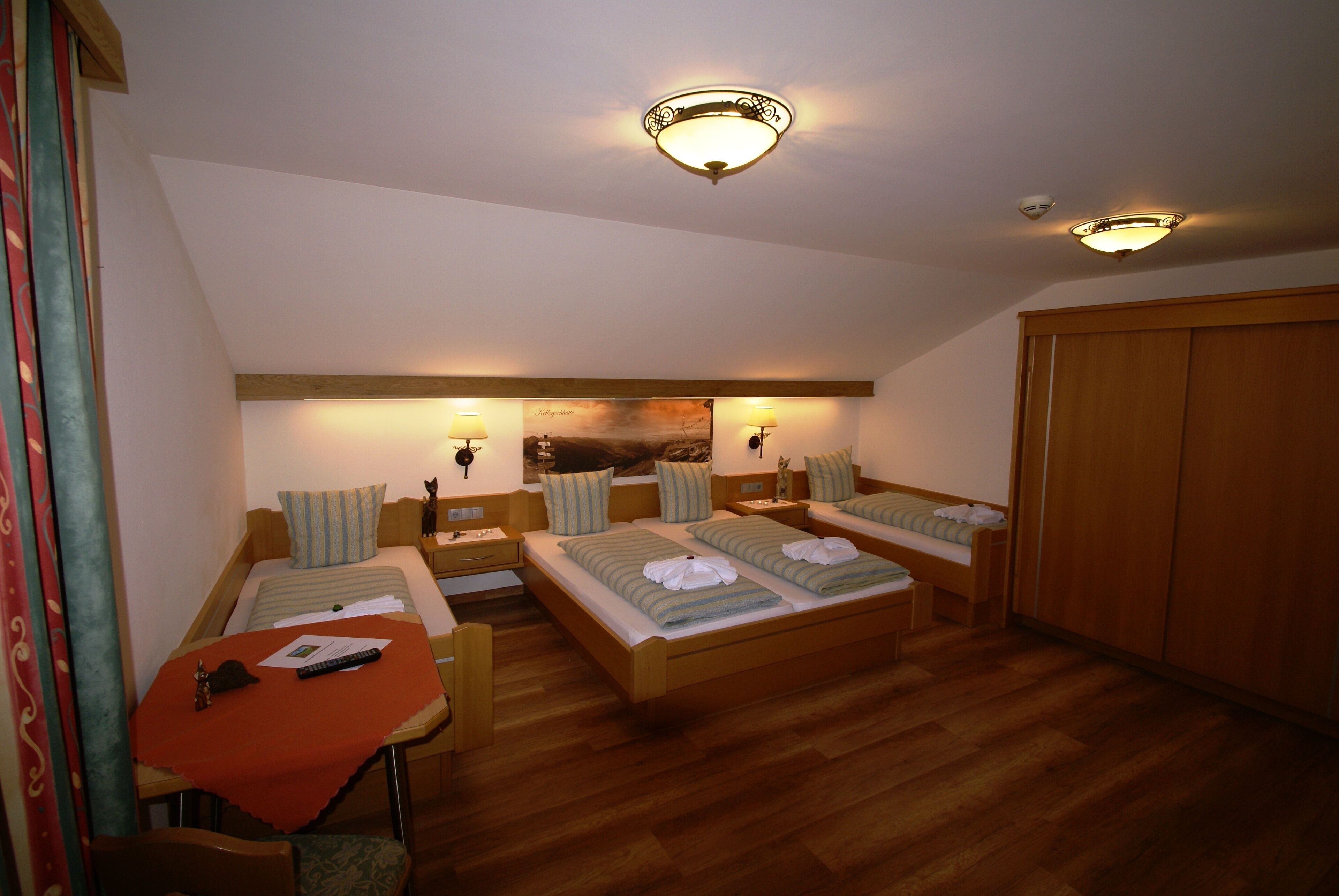 A hotel room with two single beds, a small table with a red tablecloth, a chair, and a wooden wardrobe.