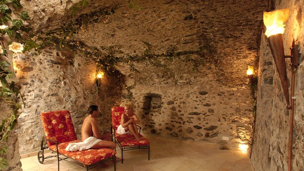 Ein Zimmer mit Steinwänden, zwei roten Blumenstühlen, einem gefliesten Boden und Wandleuchten.