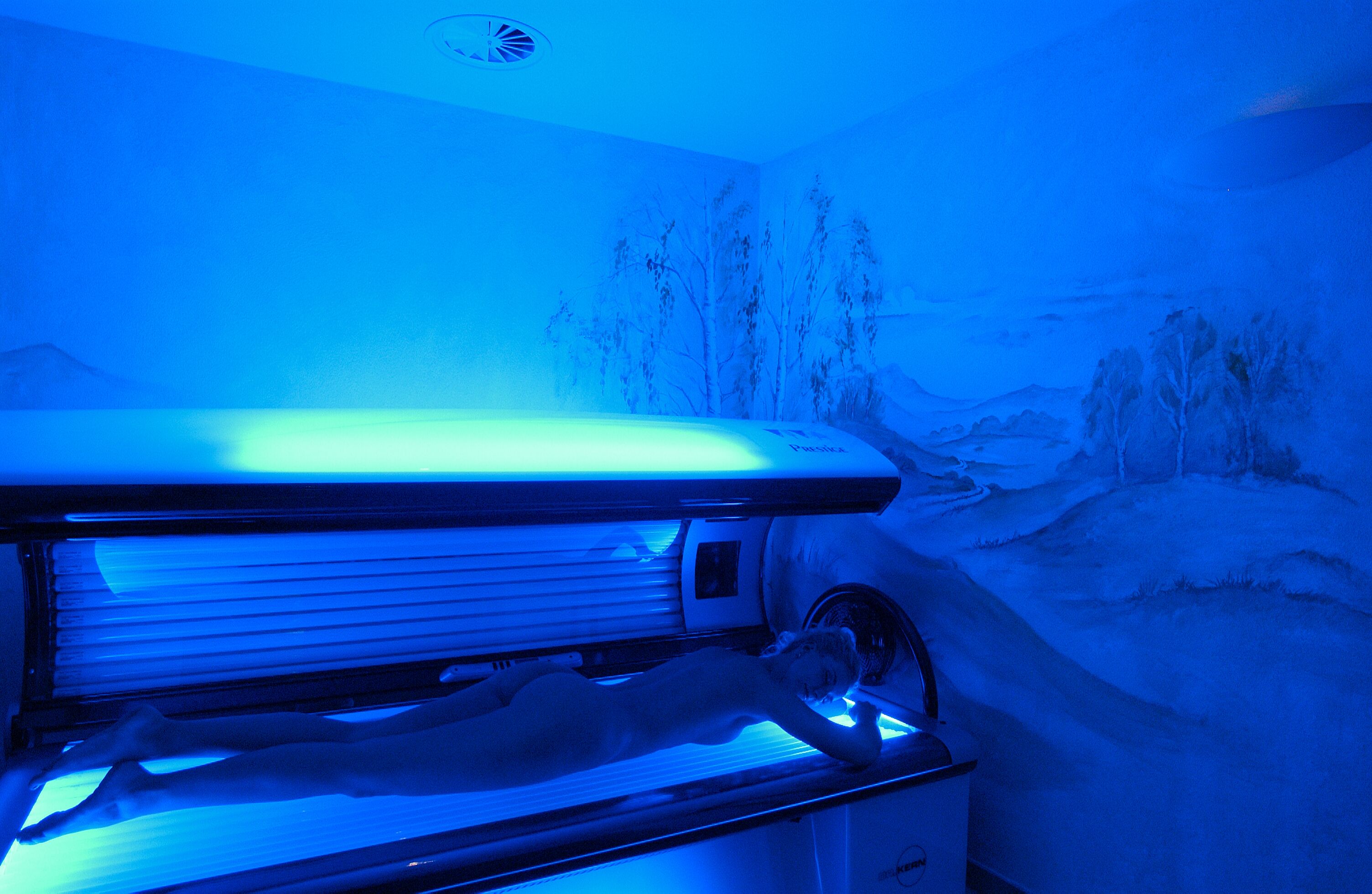 Un appareil de bronzage dans une pièce dont un mur est décoré d’une fresque représentant un paysage enneigé.