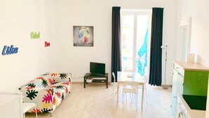 A bright living room with a colorful sofa, a dining table with chairs, a TV on a stand, and a painting on the wall. - La piazzetta - Naples (Napoli)