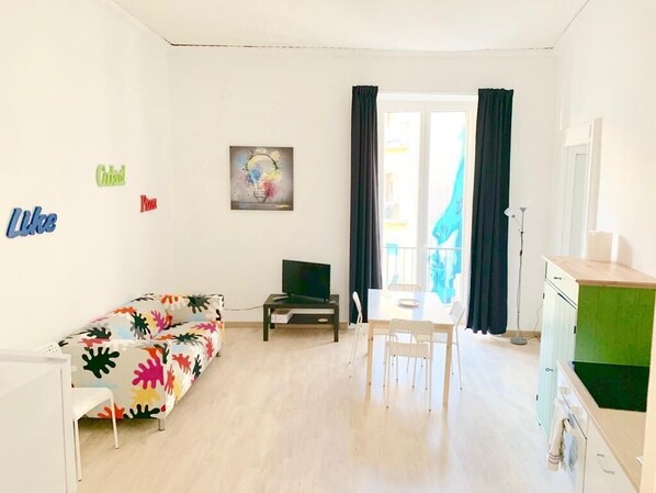 A bright living room with a colorful sofa, a dining table with chairs, a TV on a stand, and a painting on the wall. - La piazzetta - Naples (Napoli)