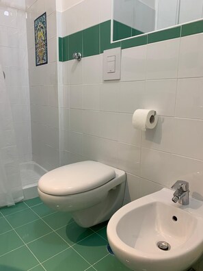 Uma casa de banho com sanita, bidé e chão em mosaico verde.