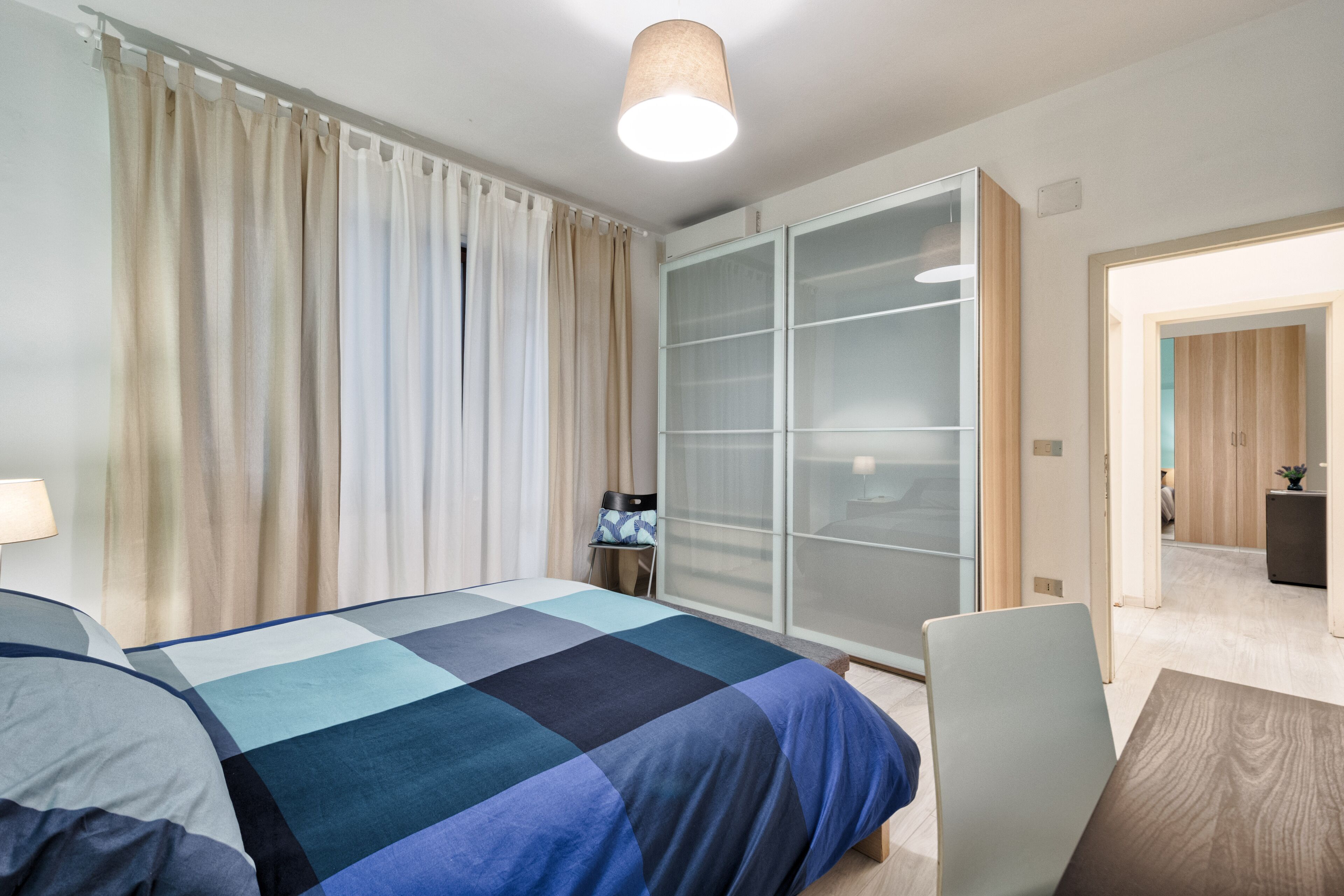 A modern hotel room with a large bed, a desk, and a wardrobe.