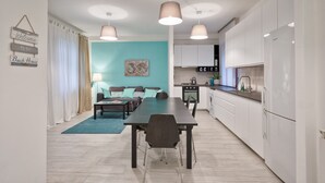 A modern kitchen with white cabinets, a dining area with a table and chairs, and a living room with a sofa and curtains.