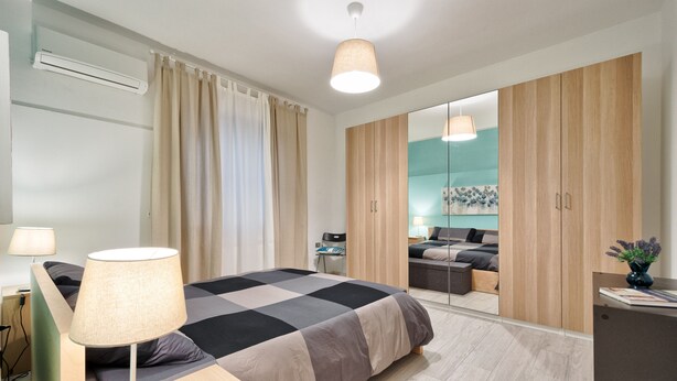 A modern bedroom with a large bed, a desk, a chair, and a wardrobe.