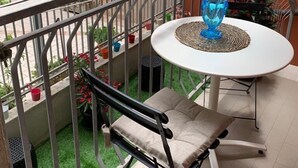 A balcony with a white table, blue vase, and a folding chair.