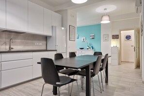 A modern kitchen with white cabinets, a black dining table, and chairs. There is a blue accent wall and a pendant light above the table.