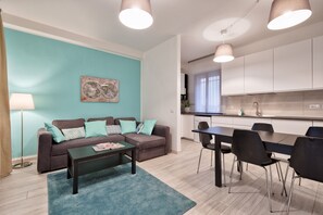 A modern apartment with a teal accent wall, a sofa set, a dining table with chairs, and a kitchen area.