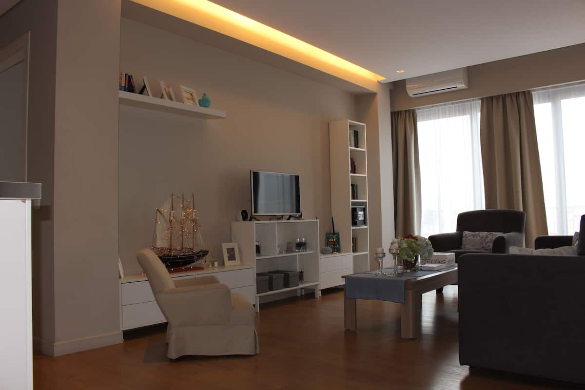 A modern living room with a sofa, armchair, TV, and shelves.