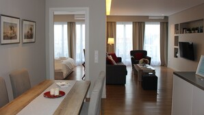 Quarto de hotel moderno com área de refeições, sofá, televisão e cama.
