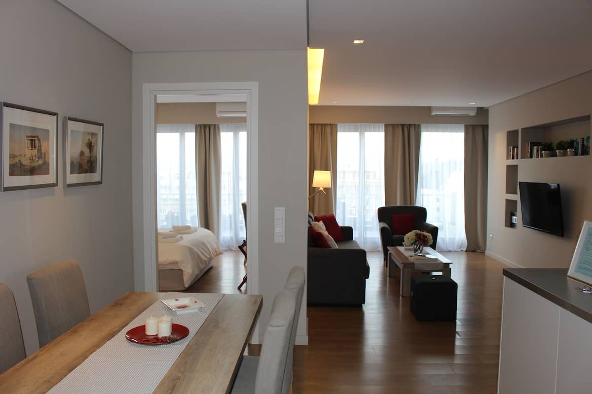 A modern hotel room with a dining area, a sofa, a TV, and a bed.