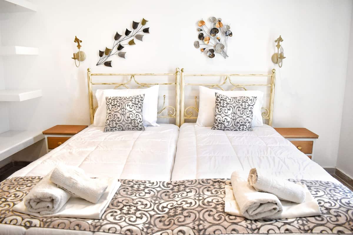 A double bed with patterned bedding, two bedside tables, decorative wall art, and a white wall.
