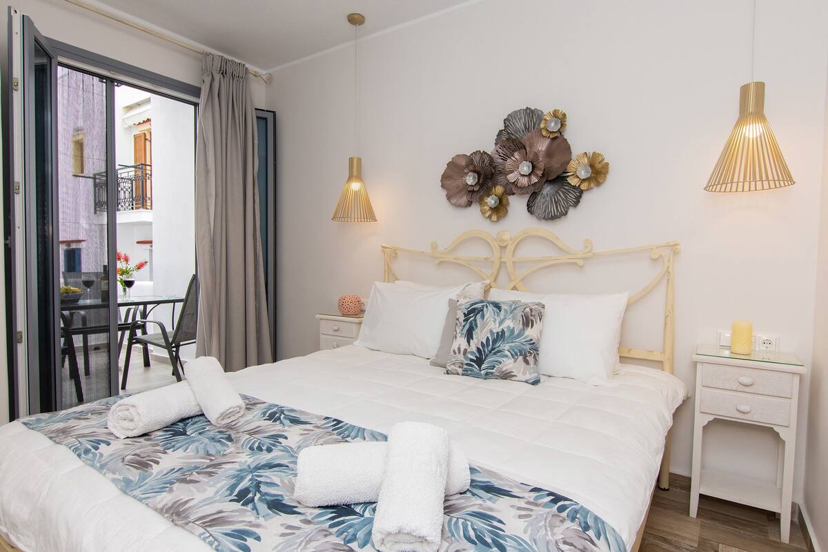 A hotel room with a bed, a nightstand, a chair, and a view of the outside balcony.