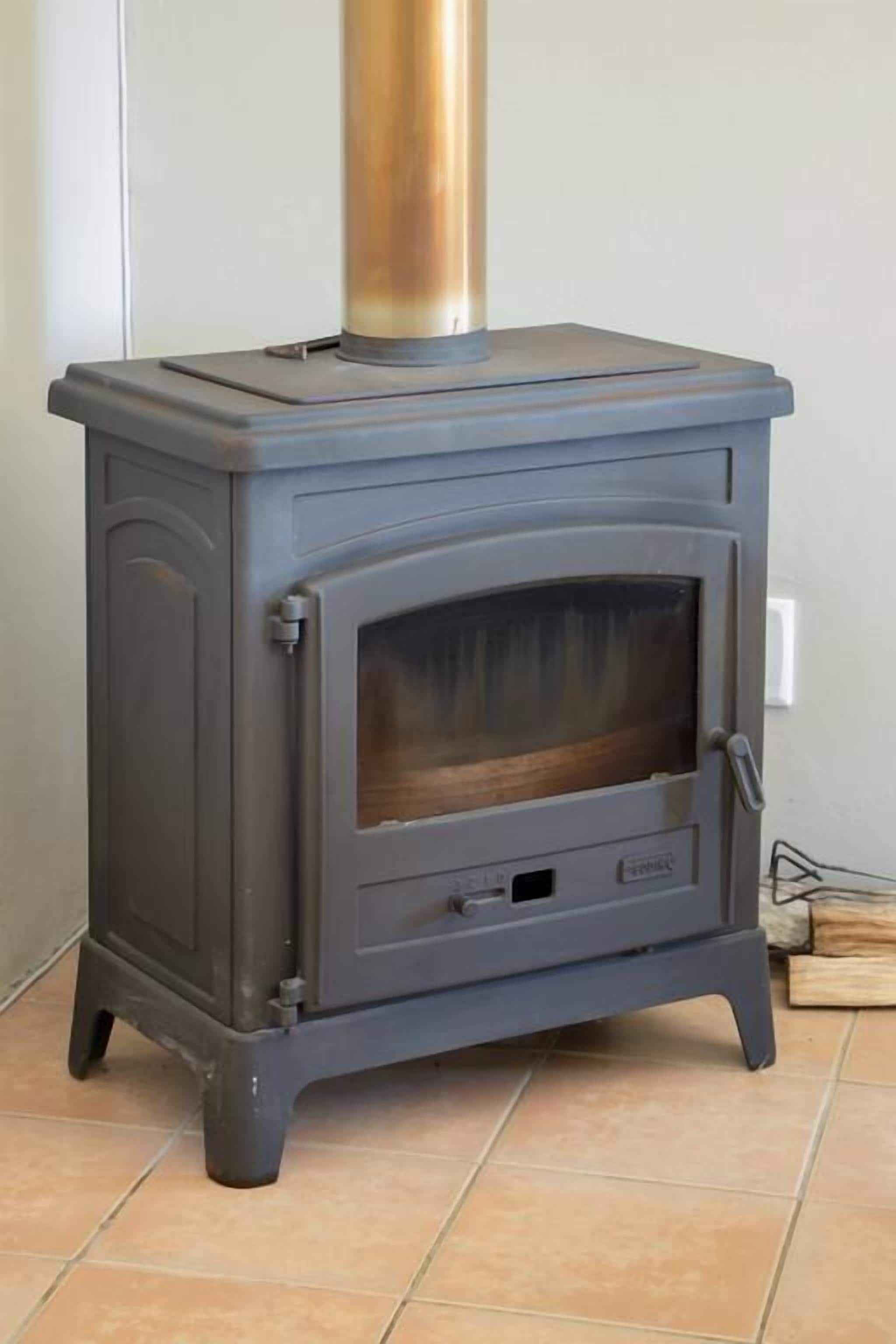 Una estufa de leña gris con puerta de vidrio y chimenea de metal.