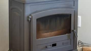 Una estufa de leña gris con puerta de vidrio y chimenea de metal.