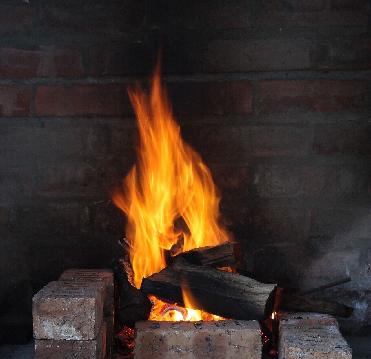 A fireplace with burning logs and a brick wall in the background.