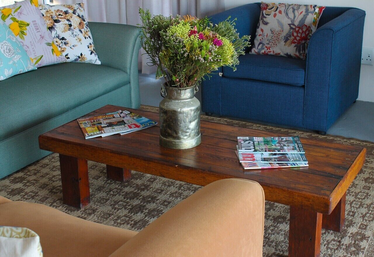 Un salón con una mesa de centro de madera, un jarrón con flores, un sofá azul y cojines estampados.