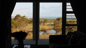 A room with a large window offering a view of a rural landscape, including trees, a pond, and a distant body of water. - Groeneweide (Gansbaai)