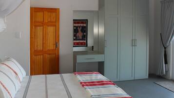 Un dormitorio con cama, puerta de madera, escritorio, armario y un cuadro en la pared.