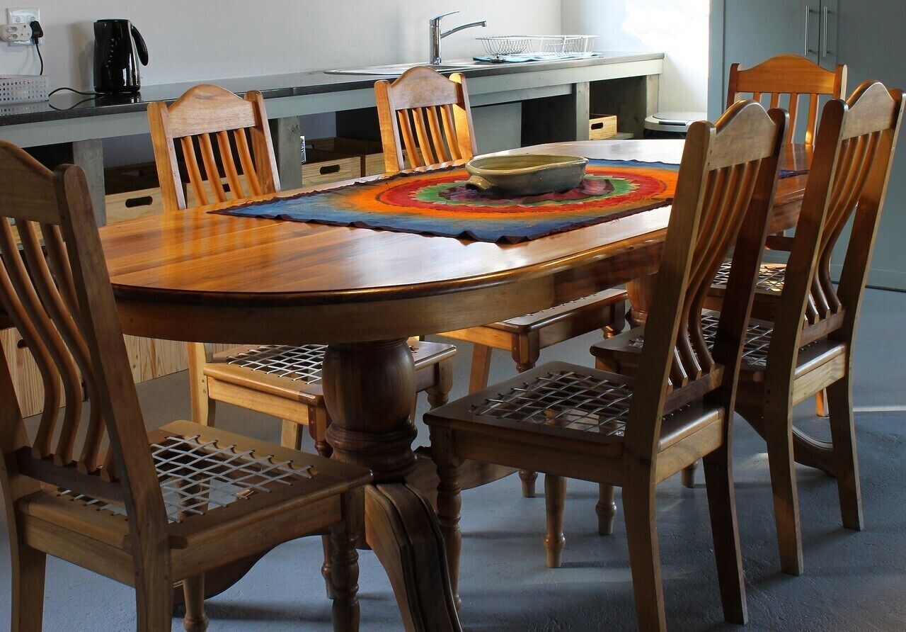 Un comedor con una mesa y sillas de madera, una cafetera y una cocina al fondo.