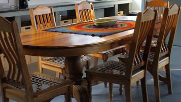 Un comedor con una mesa y sillas de madera, una cafetera y una cocina al fondo.