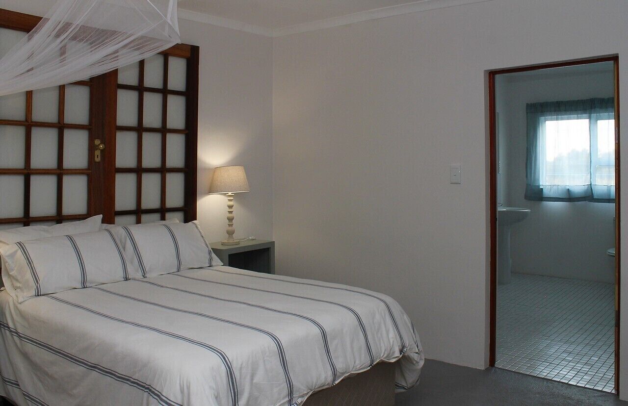 Una camera da letto con un letto, un comodino con una lampada, una finestra con tende e una porta che dà su un bagno.