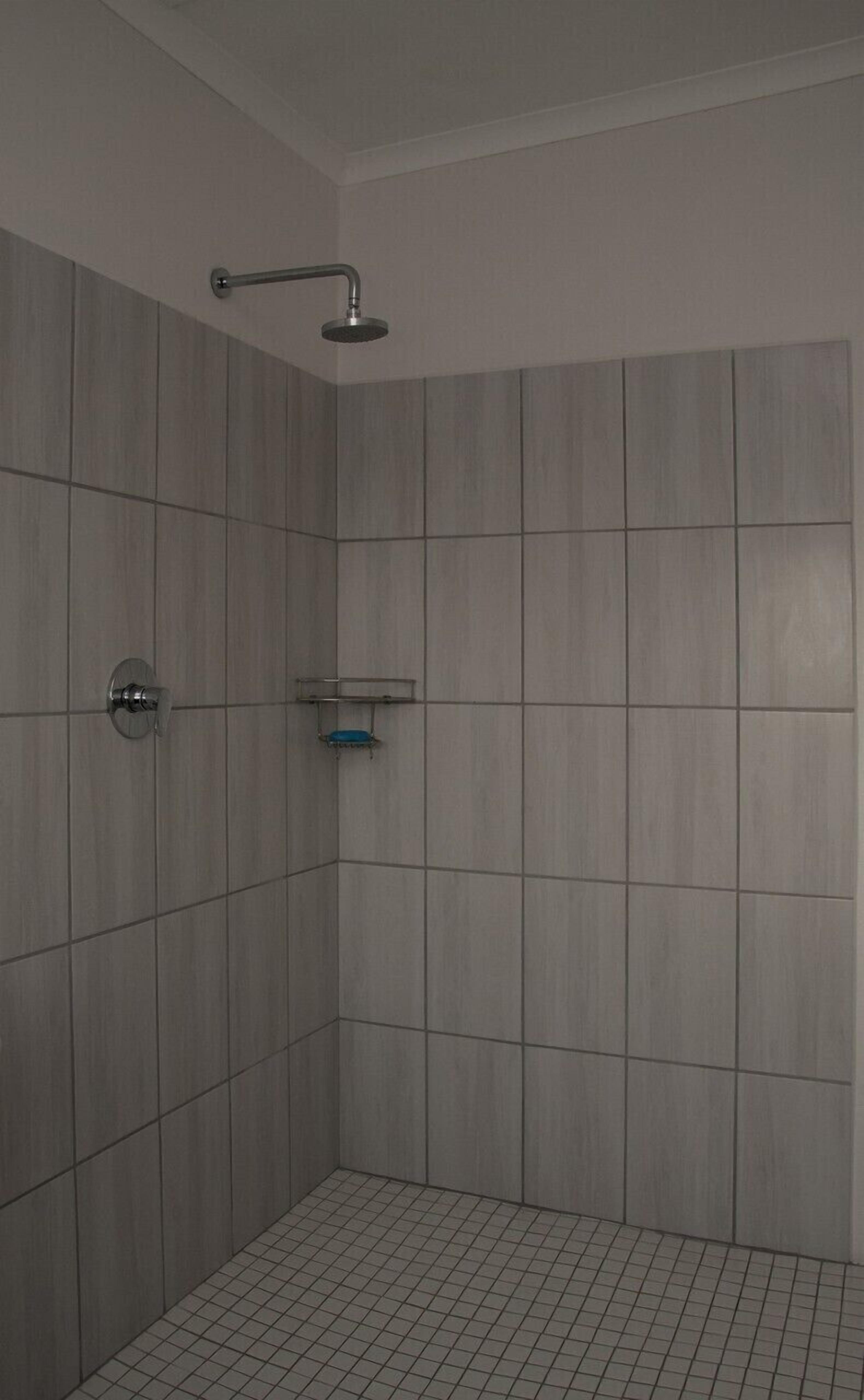 Um pequeno banheiro revestido com azulejos, com chuveiro e saboneteira.