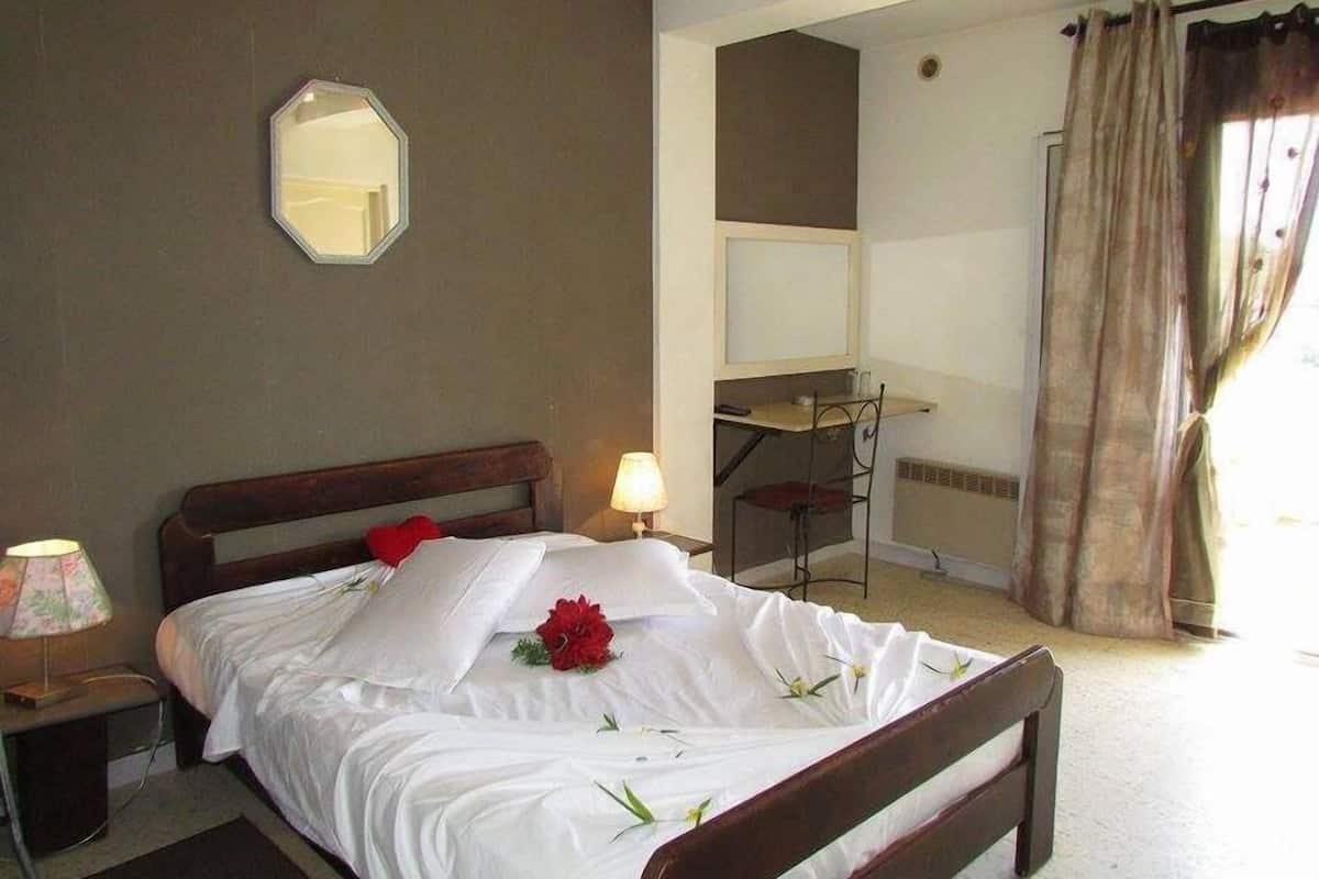 A hotel room with a bed, a desk, a chair, a mirror, and a window with curtains.