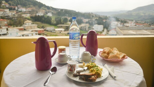 Una mesa con alimentos para el desayuno, una botella de agua y una vista de un pueblo y colinas al fondo.