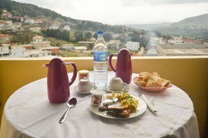 Uma mesa com itens de café da manhã, uma garrafa de água e vista para uma cidade e colinas ao fundo.