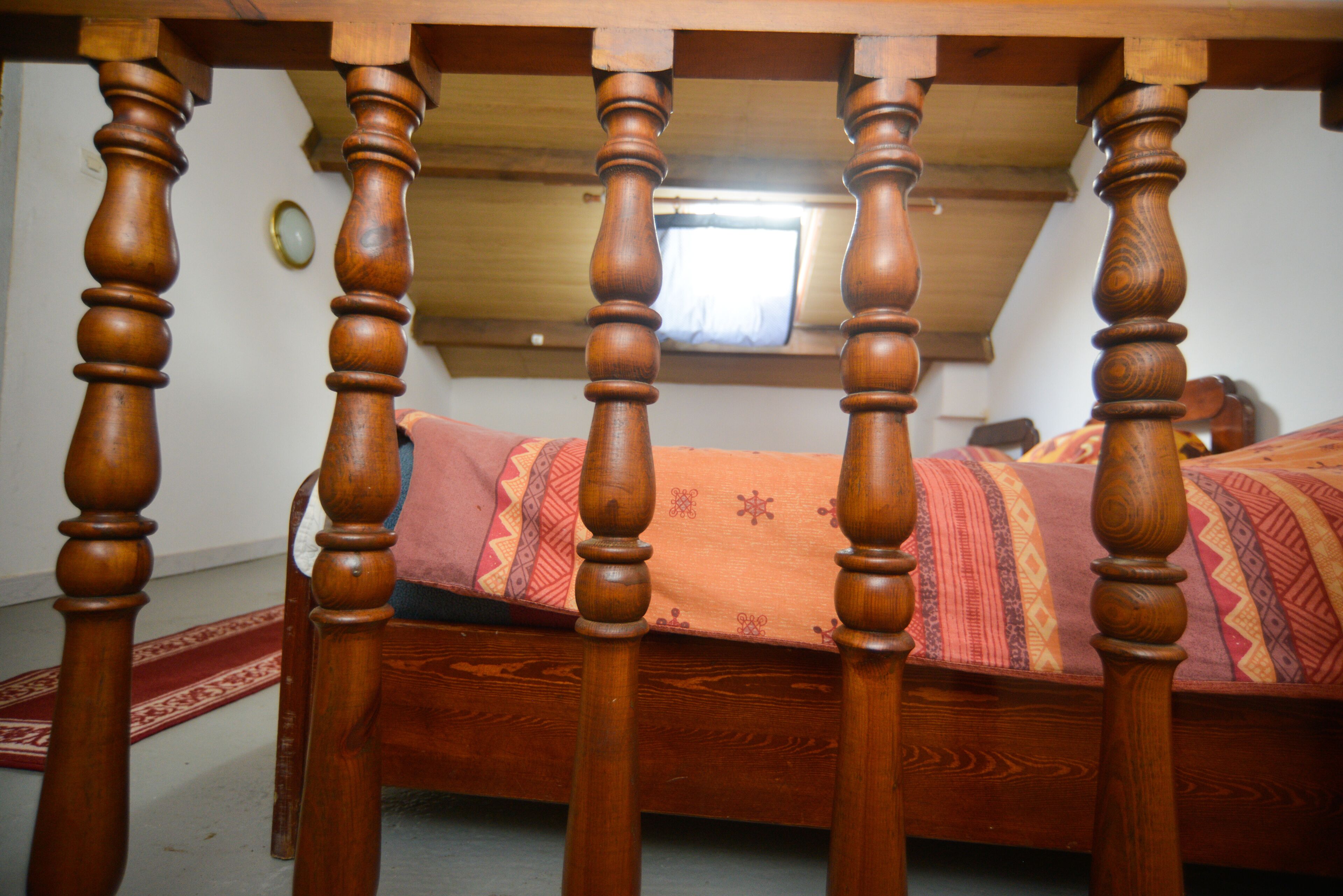 Una camera da letto con una struttura letto in legno, una coperta a motivi e una finestra che si affaccia sul cielo.