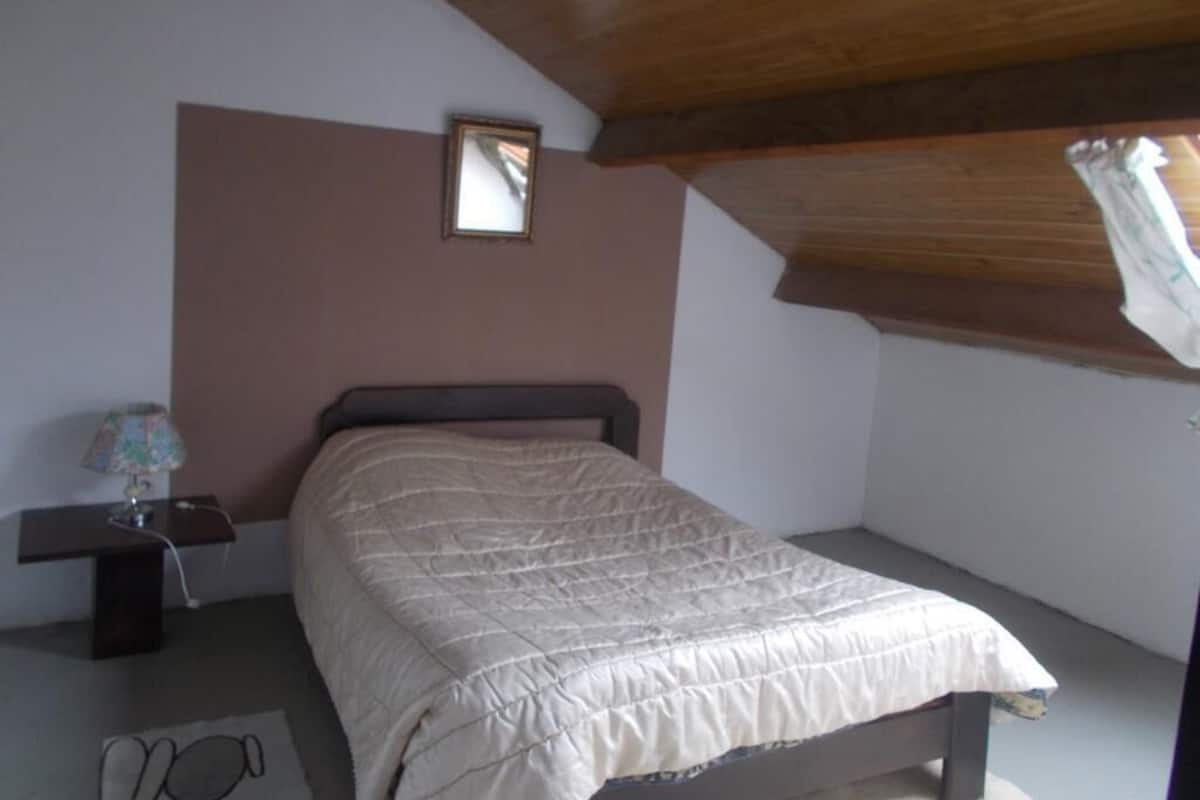 A bedroom with a bed, a nightstand, a lamp, and a window.