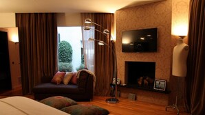 A hotel room with a large bed, a sofa with cushions, a flat-screen TV mounted on the wall, a fireplace, and a desk with a lamp. - Magnificent high-rise penthouse in Barcelona (Barcelona)