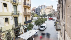 Vista de una calle con una furgoneta blanca estacionada en la vereda, edificios con balcones y mesas al aire libre en un café.