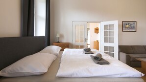 Ein Hotelzimmer mit einem Bett, einem Nachttisch, einer Lampe, einer Tür zu einem weiteren Raum und einem Bild an der Wand.