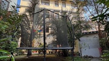 A residential area with a trampoline in a backyard, surrounded by trees and a building in the background.