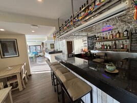 Un bar moderno con una barra larga, varios taburetes y una gran variedad de botellas y vasos.