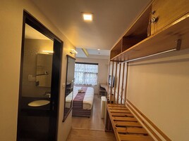 Un pasillo estrecho con una escalera de madera, una cama con manta a rayas, un espejo y una mesita con televisor.