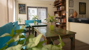 A living room with a sofa, a table, potted plants, a bookshelf, and a window with blinds. - ViaVia boutique hotel - Kathmandu (Kathmandu)