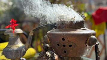 Un brûle-encens traditionnel en laiton, d’où s’échappe de la fumée, est entouré de divers aliments et d’une petite fleur rouge.