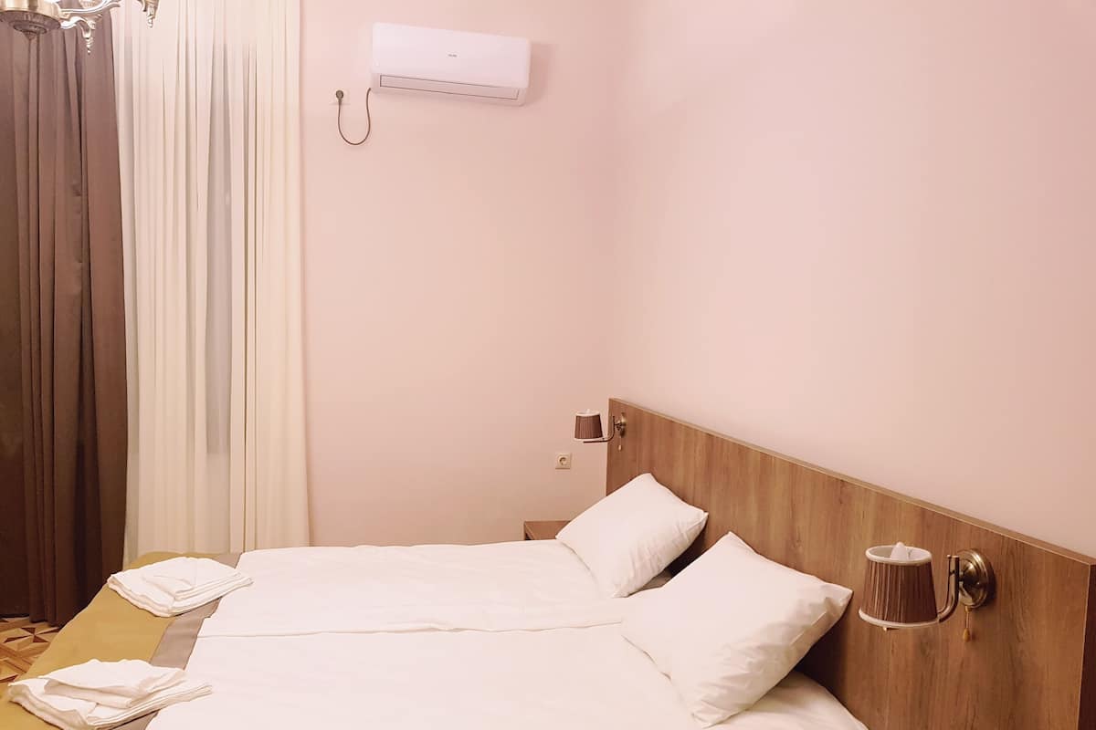 A hotel room with a bed, a bedside lamp, a telephone, and a wall-mounted air conditioner.