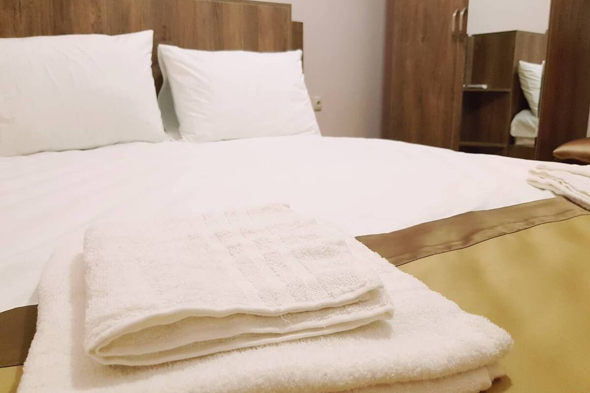 A neatly made bed with white linens and a folded white towel on the side.