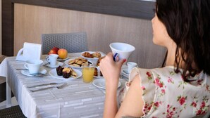Un comedor con una mesa dispuesta para el desayuno, que incluye cruasanes, fruta y un vaso de zumo de naranja.