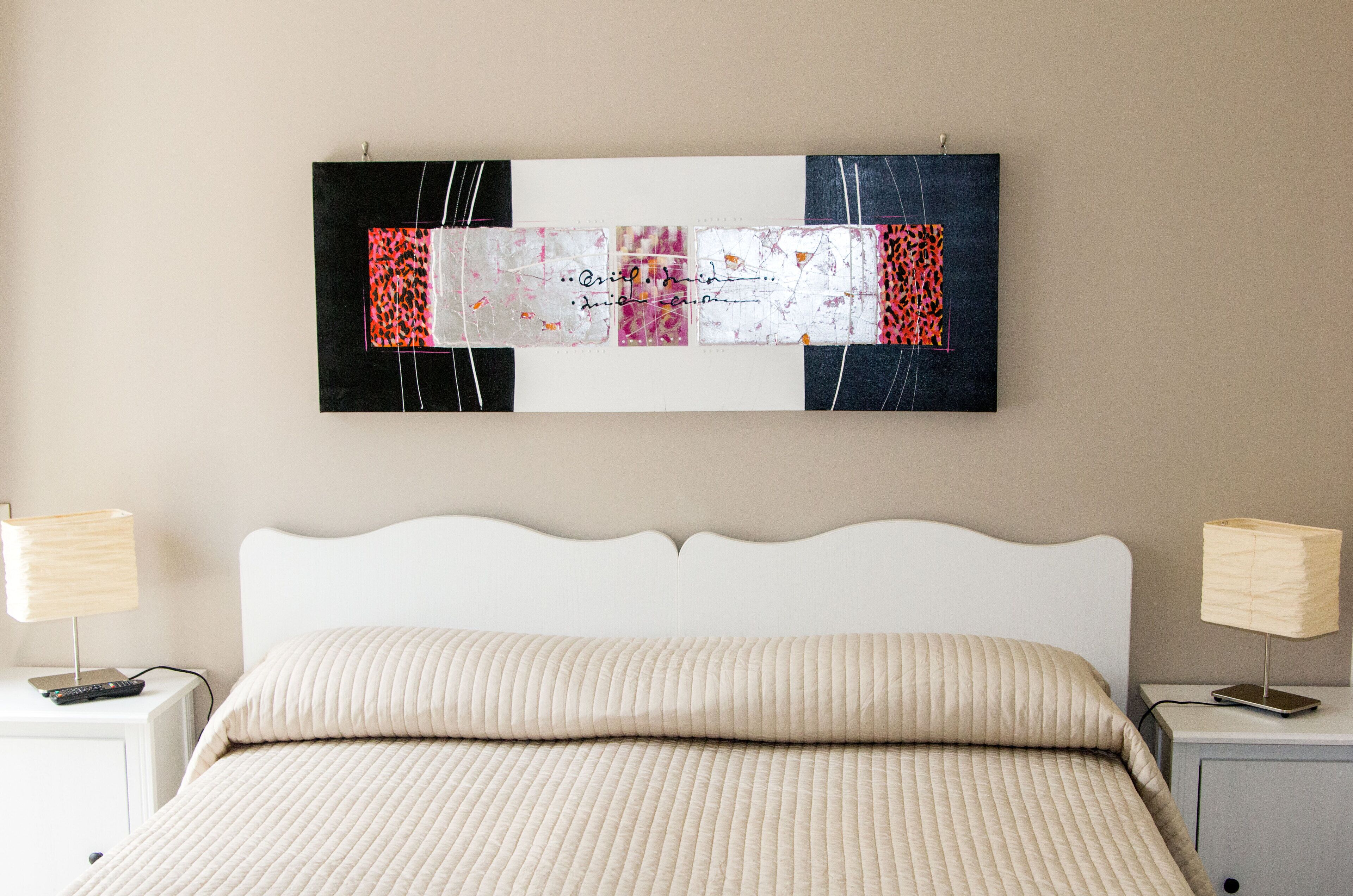 Une chambre à coucher comprenant un lit, deux tables de chevet et une œuvre d’art abstraite accrochée au mur.