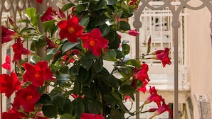 Un balcón con flores rojas y vista a un edificio histórico con una torre de reloj.