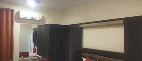 Una camera d'albergo con un letto, una scrivania, un armadio, una ventola a soffitto e un condizionatore.
