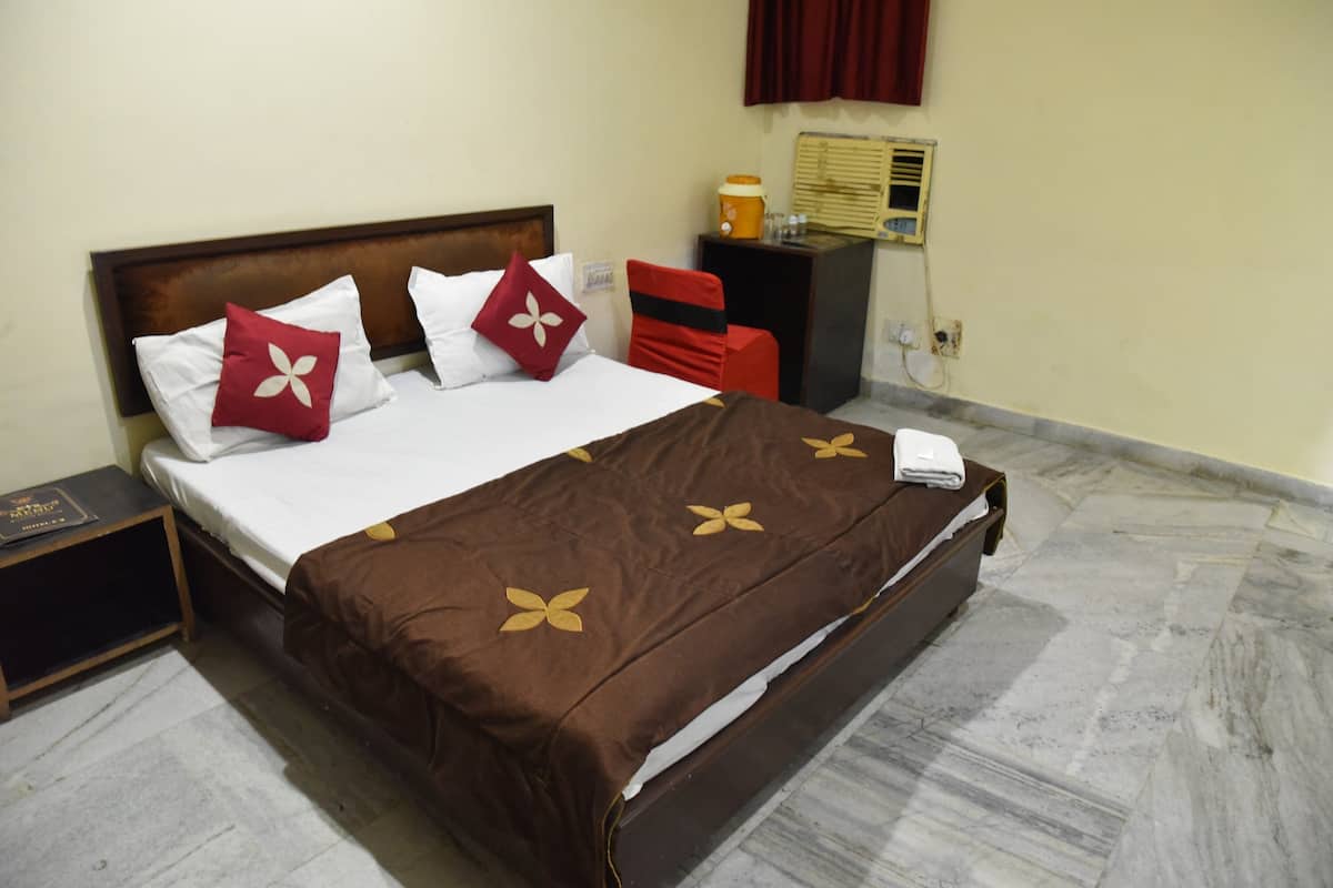 A neatly made bed with a brown bedspread and white pillows, a small bedside table with a book, and a red chair.