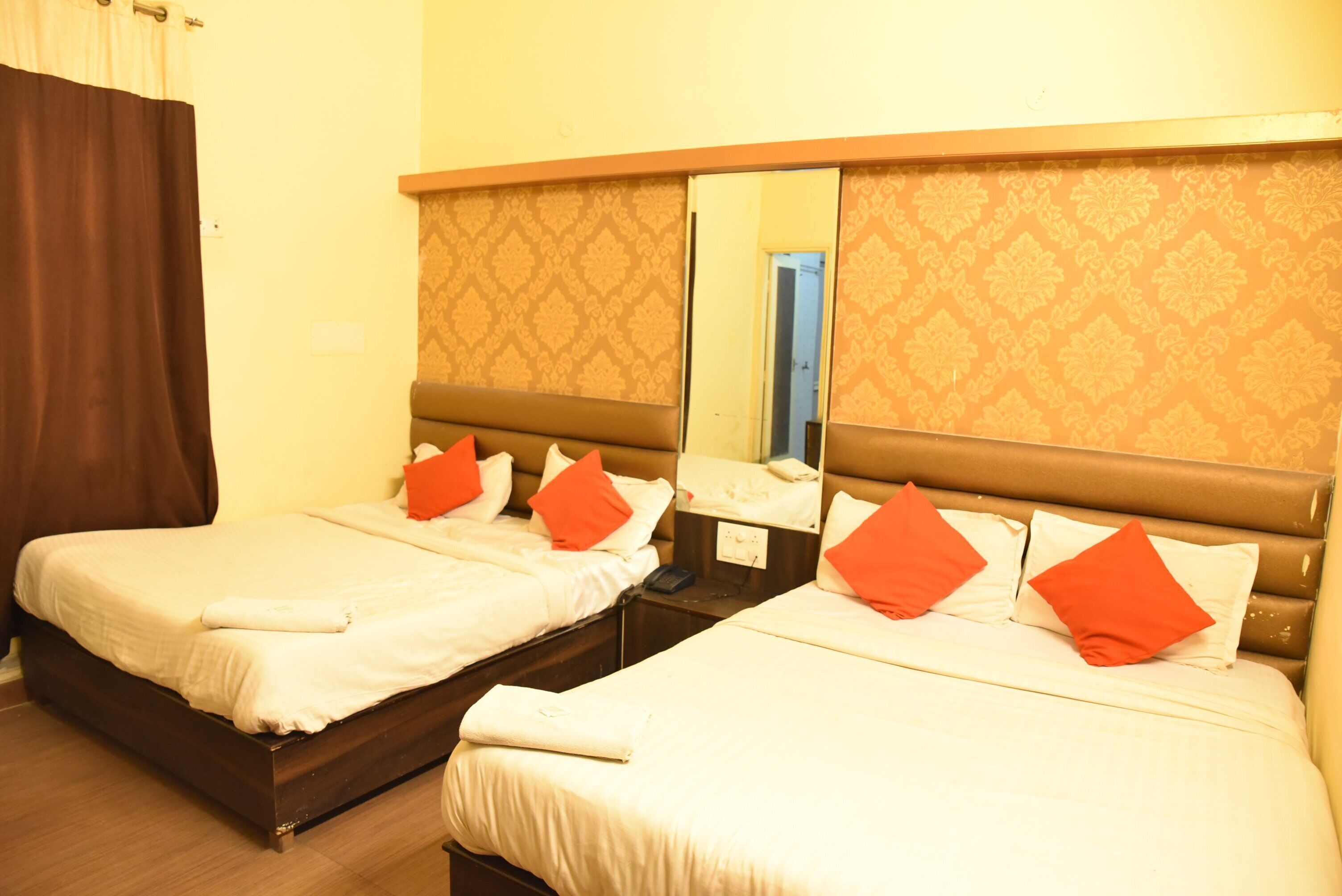 A hotel room with two beds, each with white bedding and orange pillows. There is a large mirror above the beds reflecting the room.