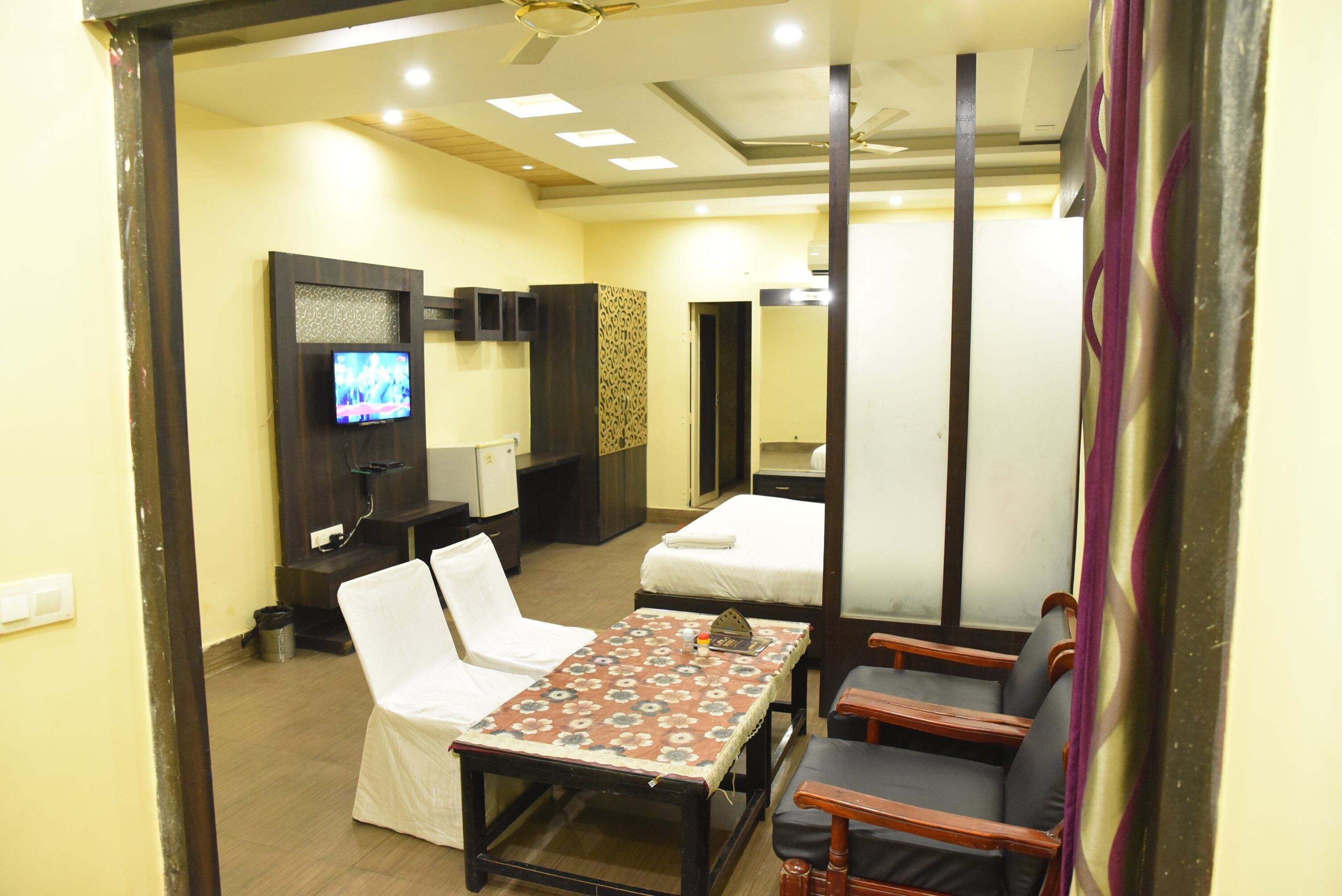 A hotel room with a bed, a TV, a table with chairs, and a mirror.