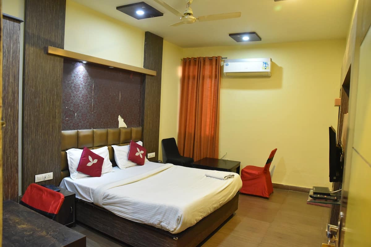 A hotel room with a bed, a desk, a chair, an air conditioning unit, and a television.